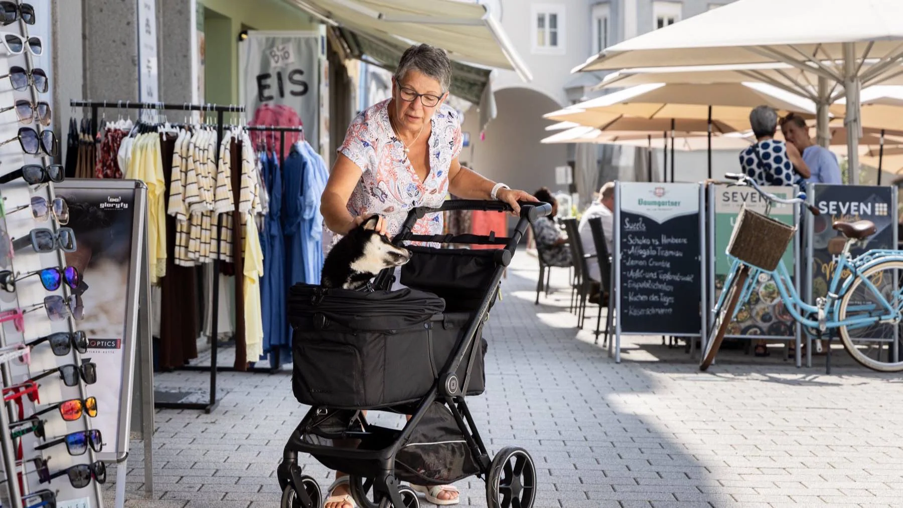Owner pushing a MOON Dog dog buggy through a pedestrian street, the dog looking out over the rim